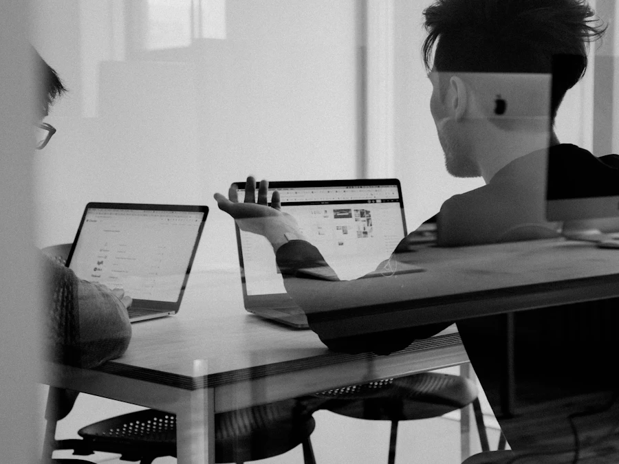 Two colleagues working on laptops seen through a glass wall